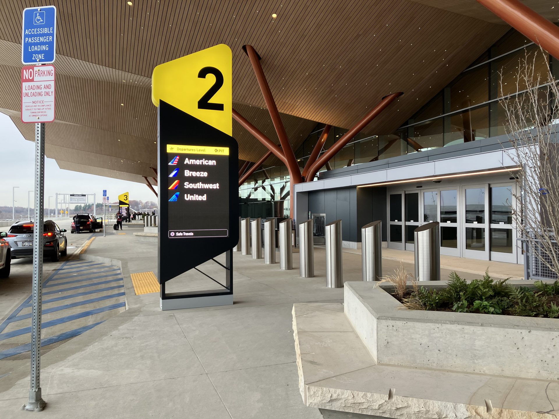 The passenger drop-off zone outside an airport terminal, with cars at the curb